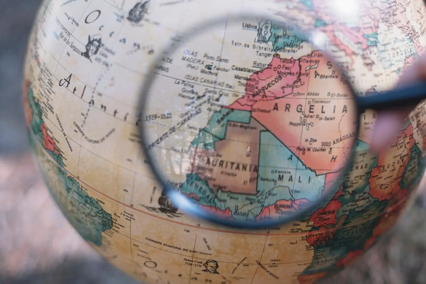 Bildausschnitt einer Hand mit Lupe über einem Globus